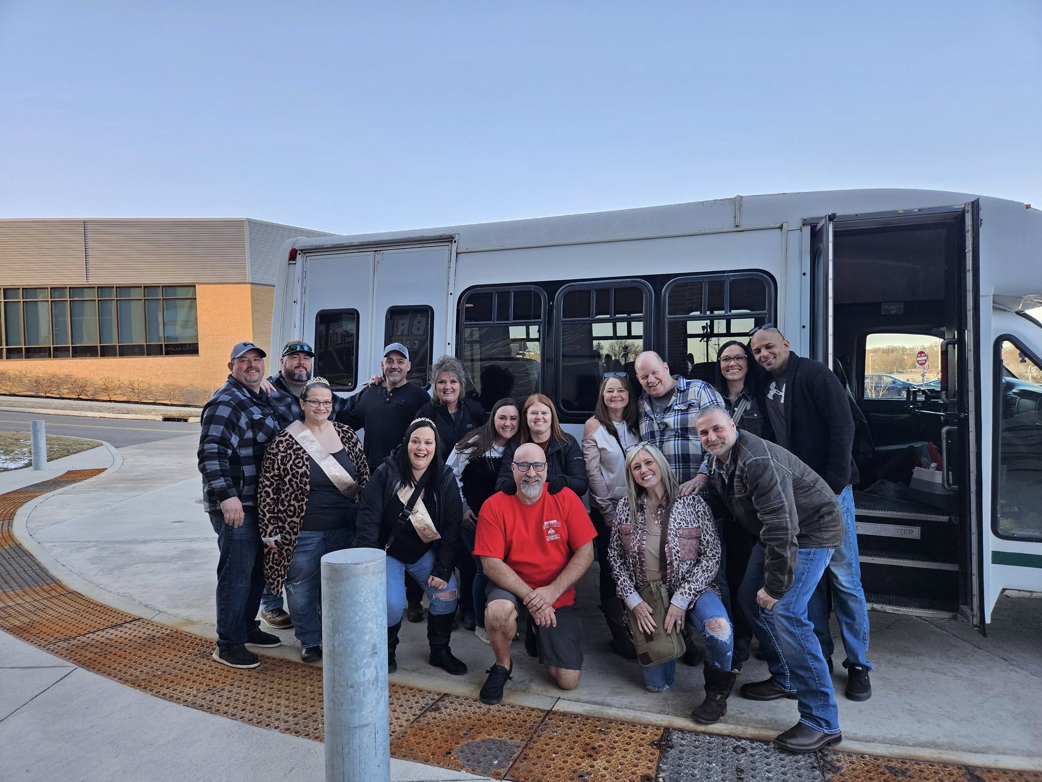 Group of about 14 passengers smiling in front of the party bus during a daytime trip