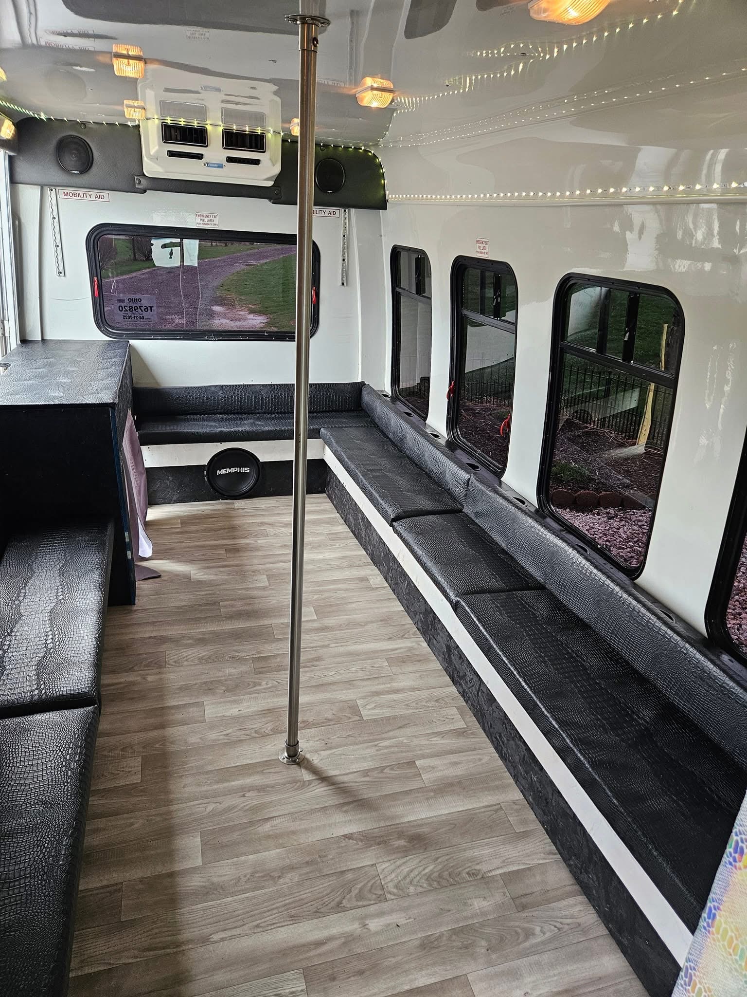 Party bus interior showing leather bench seating, dance pole, and ceiling string lights